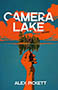 Camera Lake: cover depicting a small island full of trees and a giant camera. A hand stretches towards the island. The image is drawn in stark blue and orange, the subtlest hint of green in the trees. The title text is written in bold white font, partially obscured by the clouds over the island.